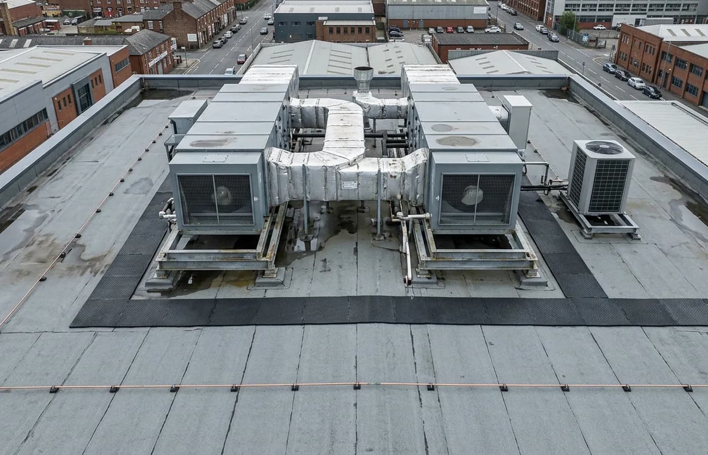 Rooftop plant on a flat commercial roof, air handling units on steel frames with ductwork and a rubber walkway route between them